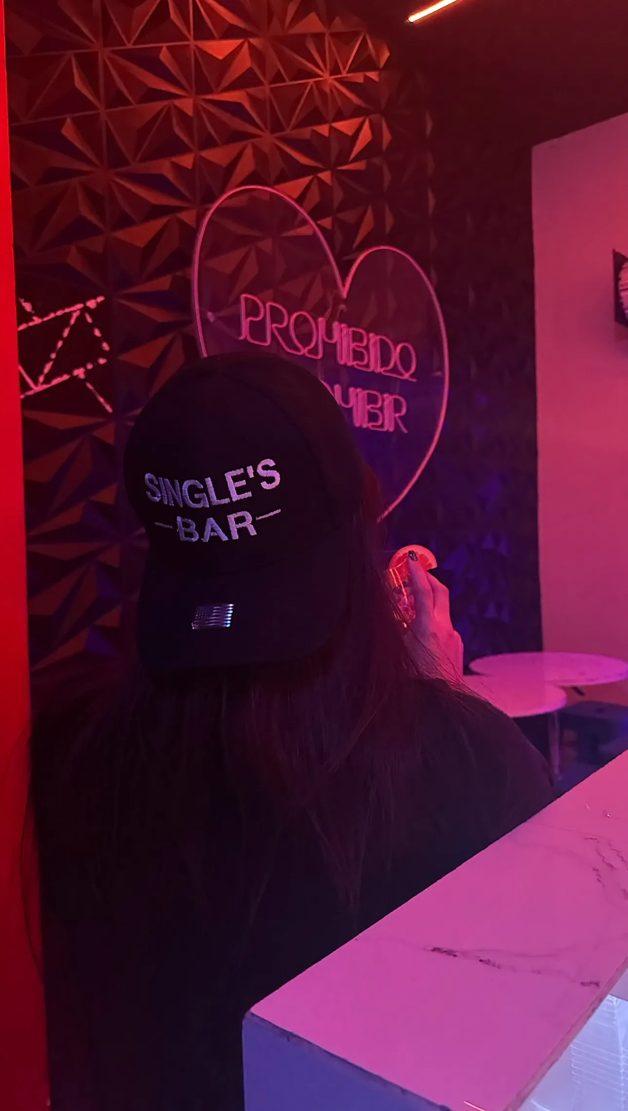 Person with a Single's Bar cap in front of neon